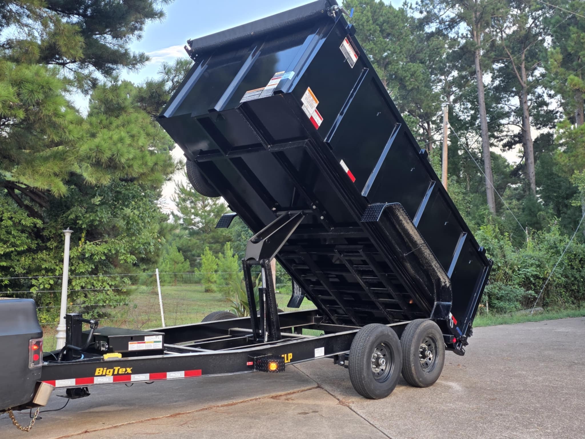 Black Big Tex dump trailer with its bed raised, parked on pavement.